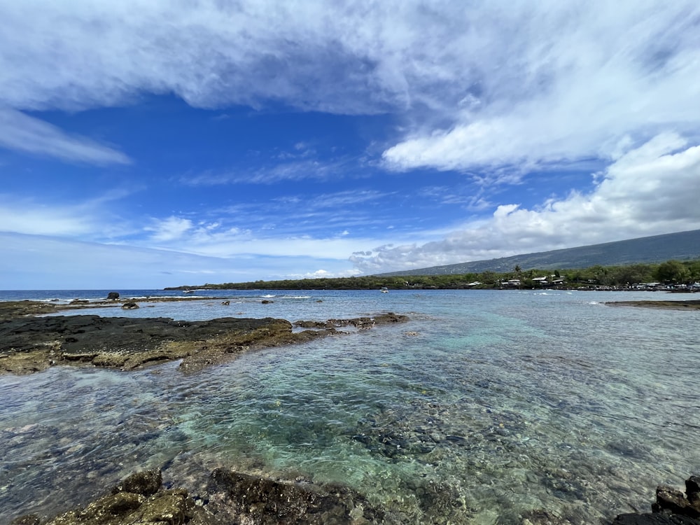 a body of water surrounded by rocks under a cloudy blue sky