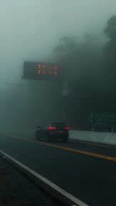um automóvel a circular numa estrada com nevoeiro e com uma placa de limite de velocidade
