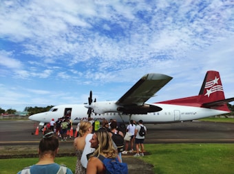 A group of people are standing in line on a runway, boarding a small aircraft with 'Air Panama' written on its side. The aircraft is white with a red tail fin that features white stars. The sky is mostly clear with a few scattered clouds.