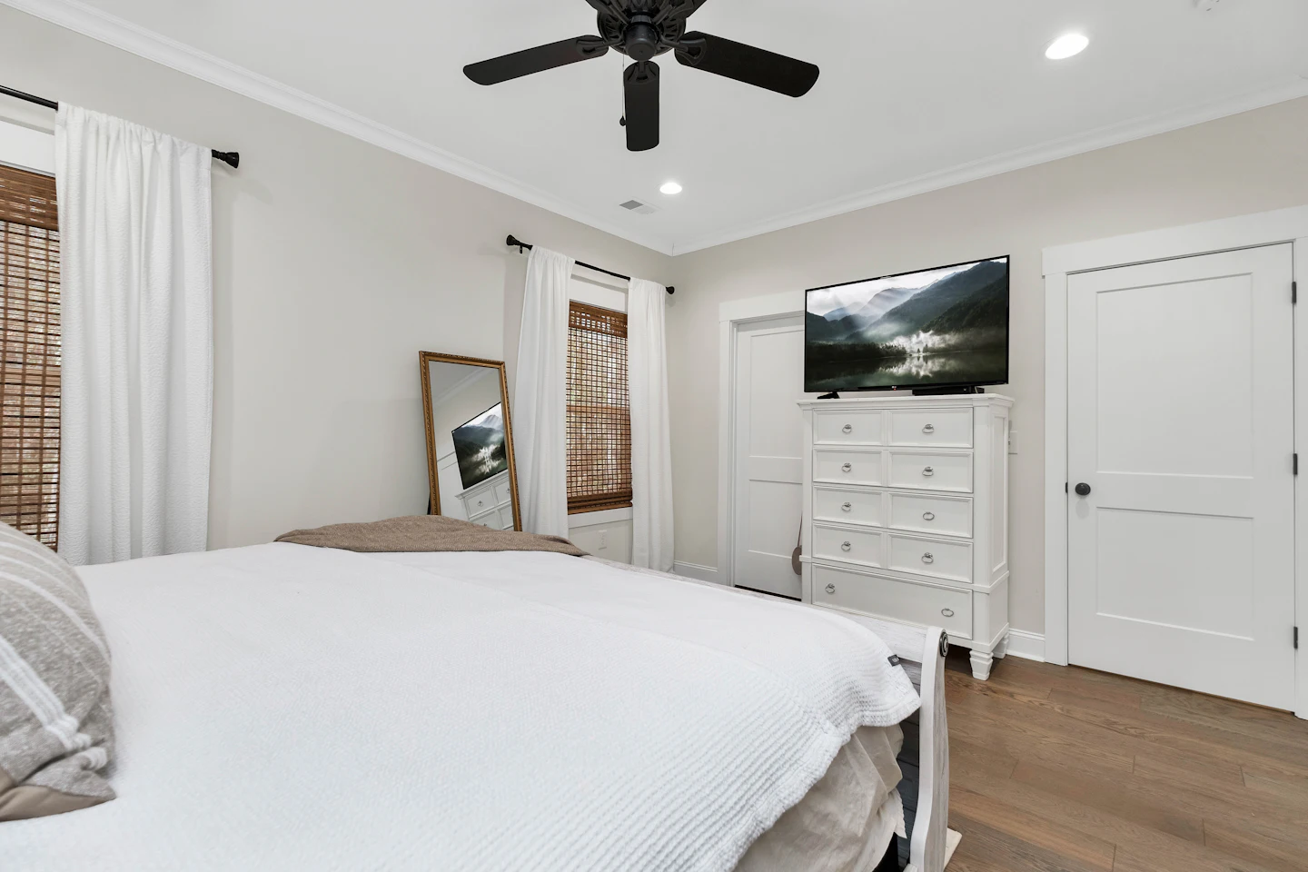Bright bedroom with white bedding, a ceiling fan and wood floors