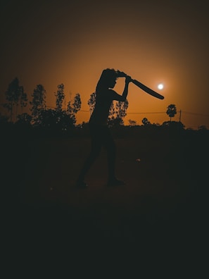 A young cricketer in mid-swing, bat raised high against a sunny pitch backdrop
