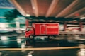 A red delivery truck is moving at high speed under an overpass on a wet road. The motion blur suggests fast movement, and the reflections on the pavement indicate recent rainfall. The truck has the word 'FORWARDERS' written on its side.