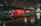 A red delivery truck moves quickly under a bridge in an urban setting at night, captured with a motion blur effect. The wet pavement reflects the lights, creating a dynamic and vibrant scene.