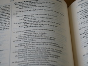 A close-up view of an open book displaying Biblical text. The pages feature chapters and verses with headings such as 'Woes and judgments' and text in a traditional font. The content includes structured, numbered lines.