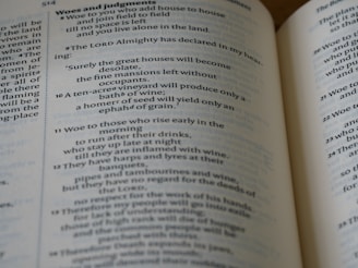 A close-up view of an open book displaying Biblical text. The pages feature chapters and verses with headings such as 'Woes and judgments' and text in a traditional font. The content includes structured, numbered lines.