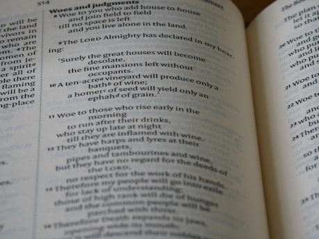 A close-up view of an open book displaying Biblical text. The pages feature chapters and verses with headings such as 'Woes and judgments' and text in a traditional font. The content includes structured, numbered lines.