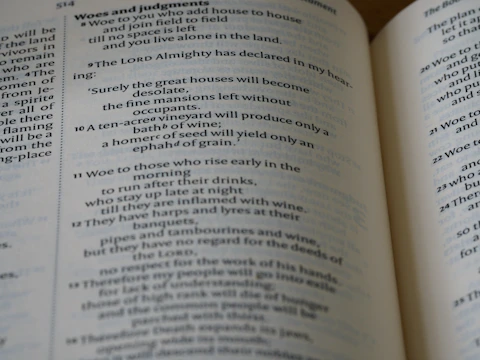 A close-up view of an open book displaying Biblical text. The pages feature chapters and verses with headings such as 'Woes and judgments' and text in a traditional font. The content includes structured, numbered lines.
