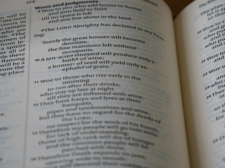 A close-up view of an open book displaying Biblical text. The pages feature chapters and verses with headings such as 'Woes and judgments' and text in a traditional font. The content includes structured, numbered lines.