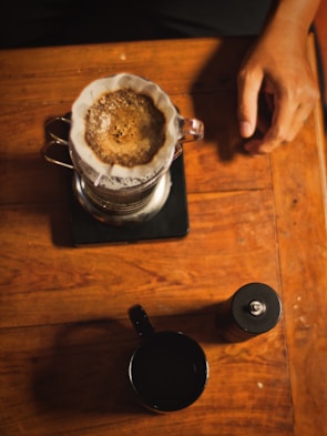 Overhead shot of a minimalist coffee setup featuring a sleek grinder and a steaming cup on a wooden table.