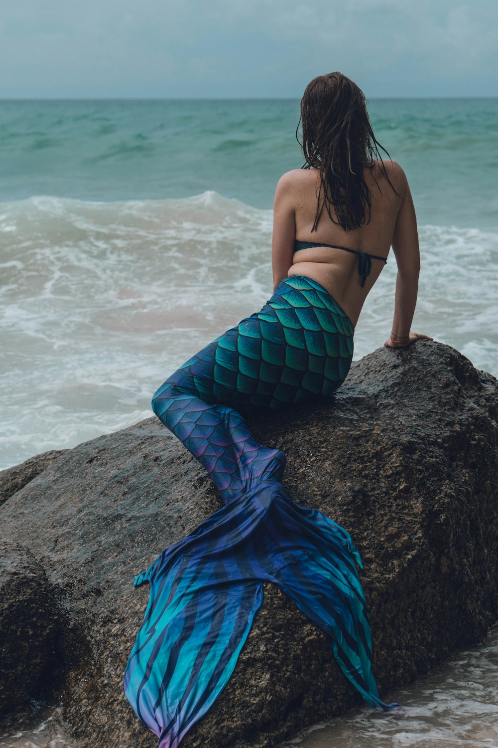 a woman is sitting on a rock by the ocean