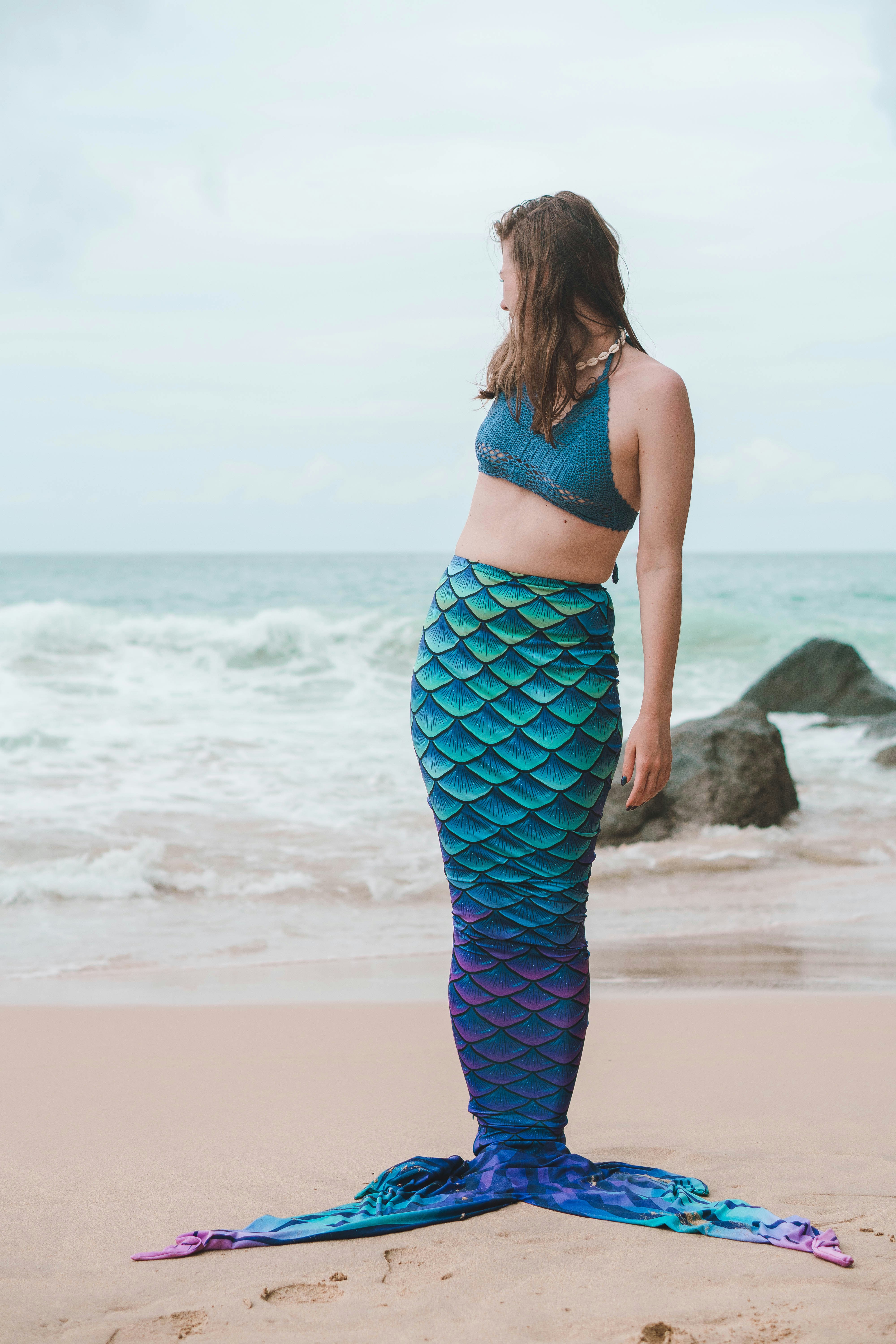a woman is standing on the beach with a mermaid tail
