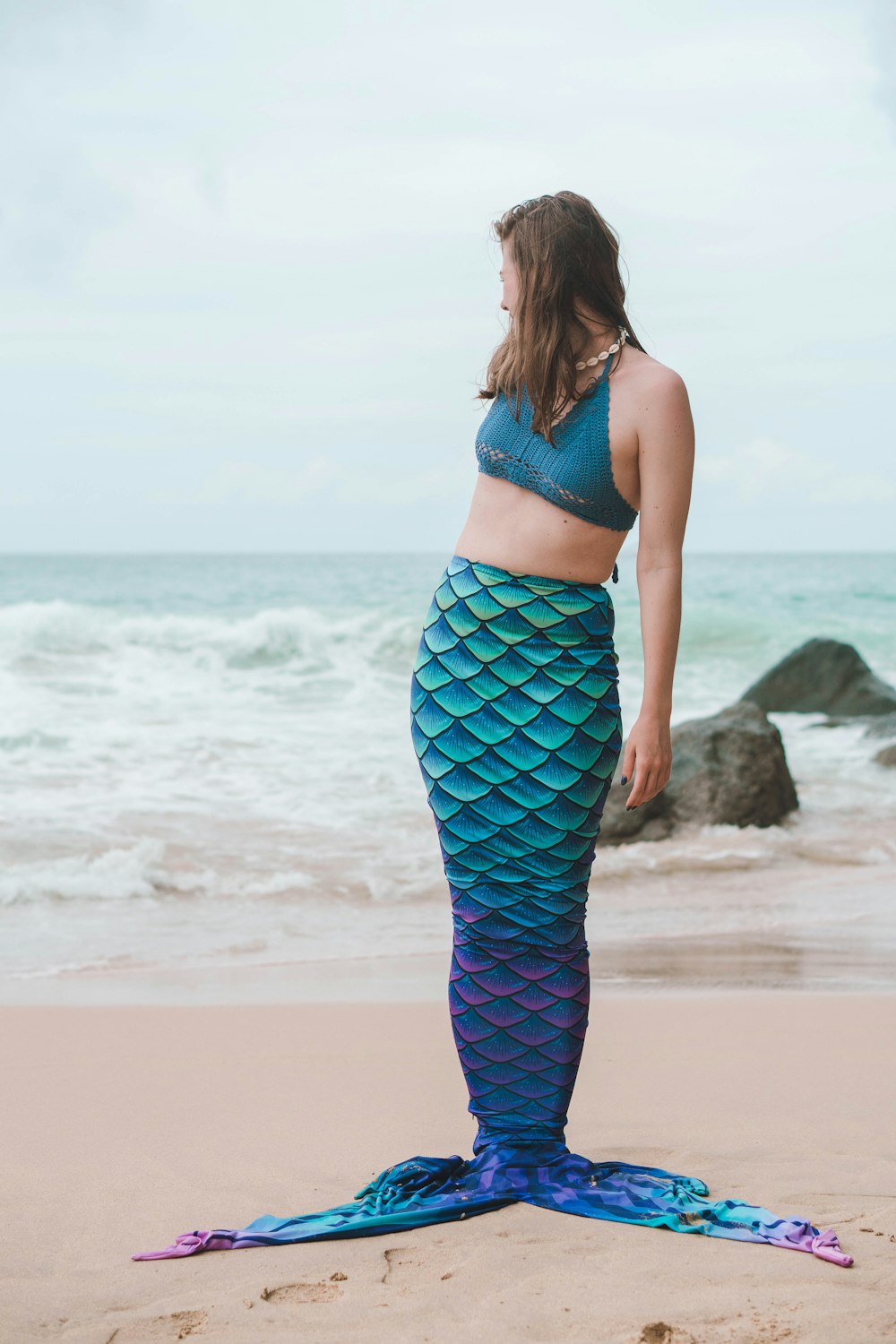 a woman is standing on the beach with a mermaid tail