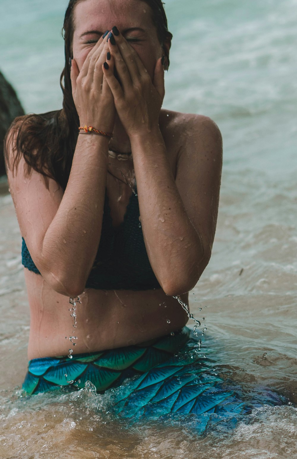 Una mujer sentada en el agua cubriéndose la cara