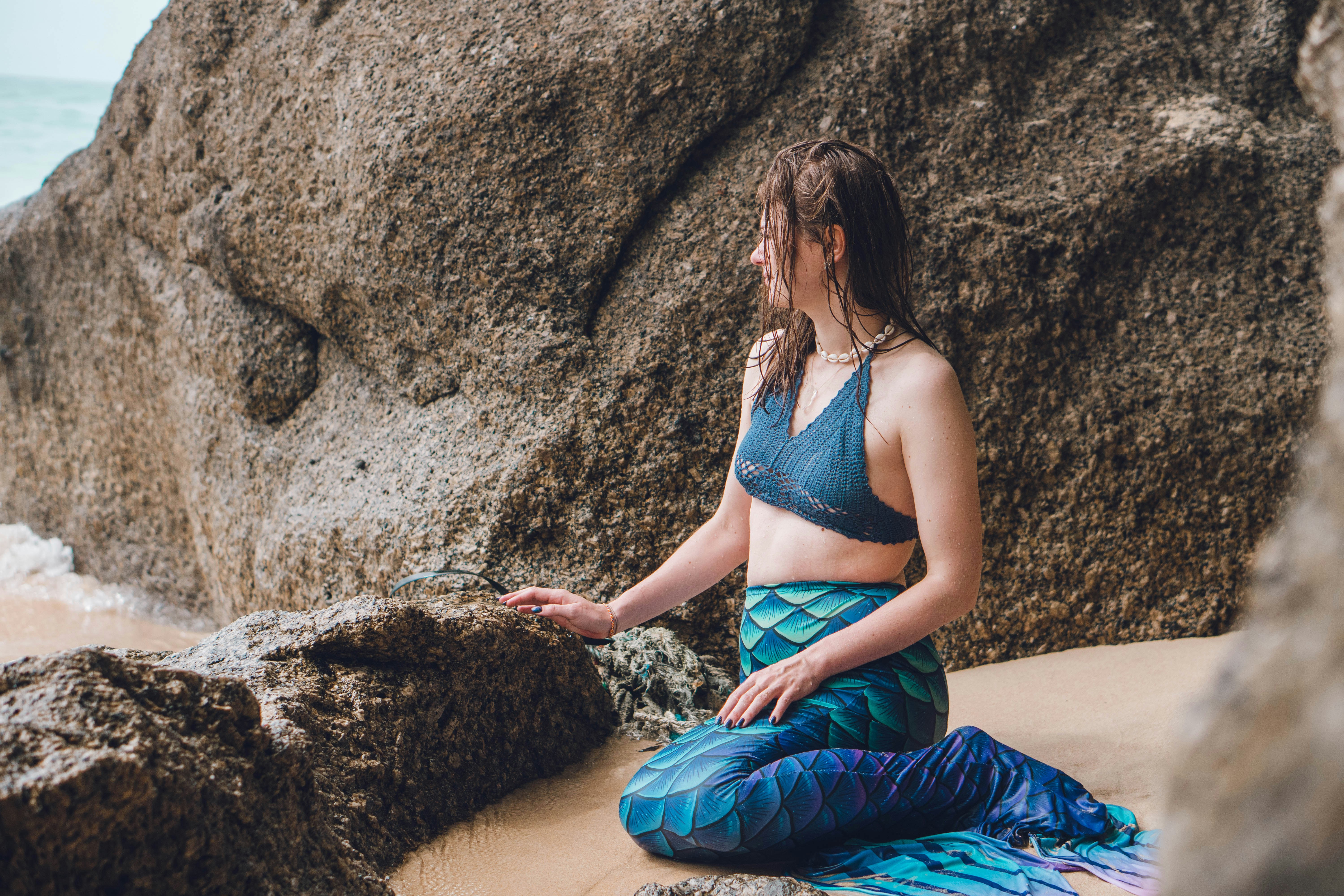 a woman in a bikini top sitting on a rock next to the ocean