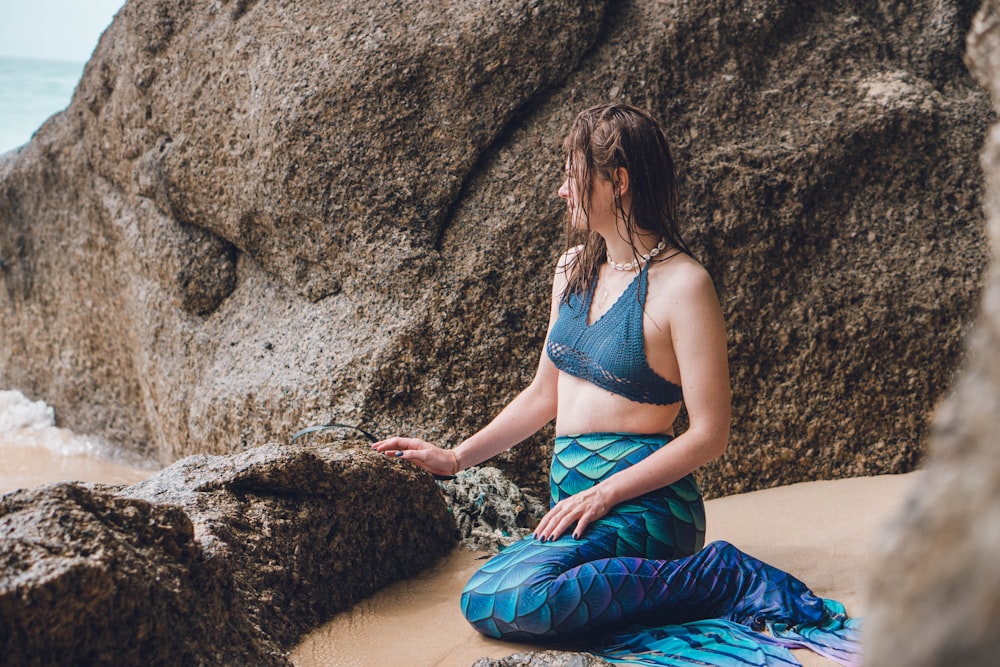 a woman in a bikini top sitting on a rock next to the ocean