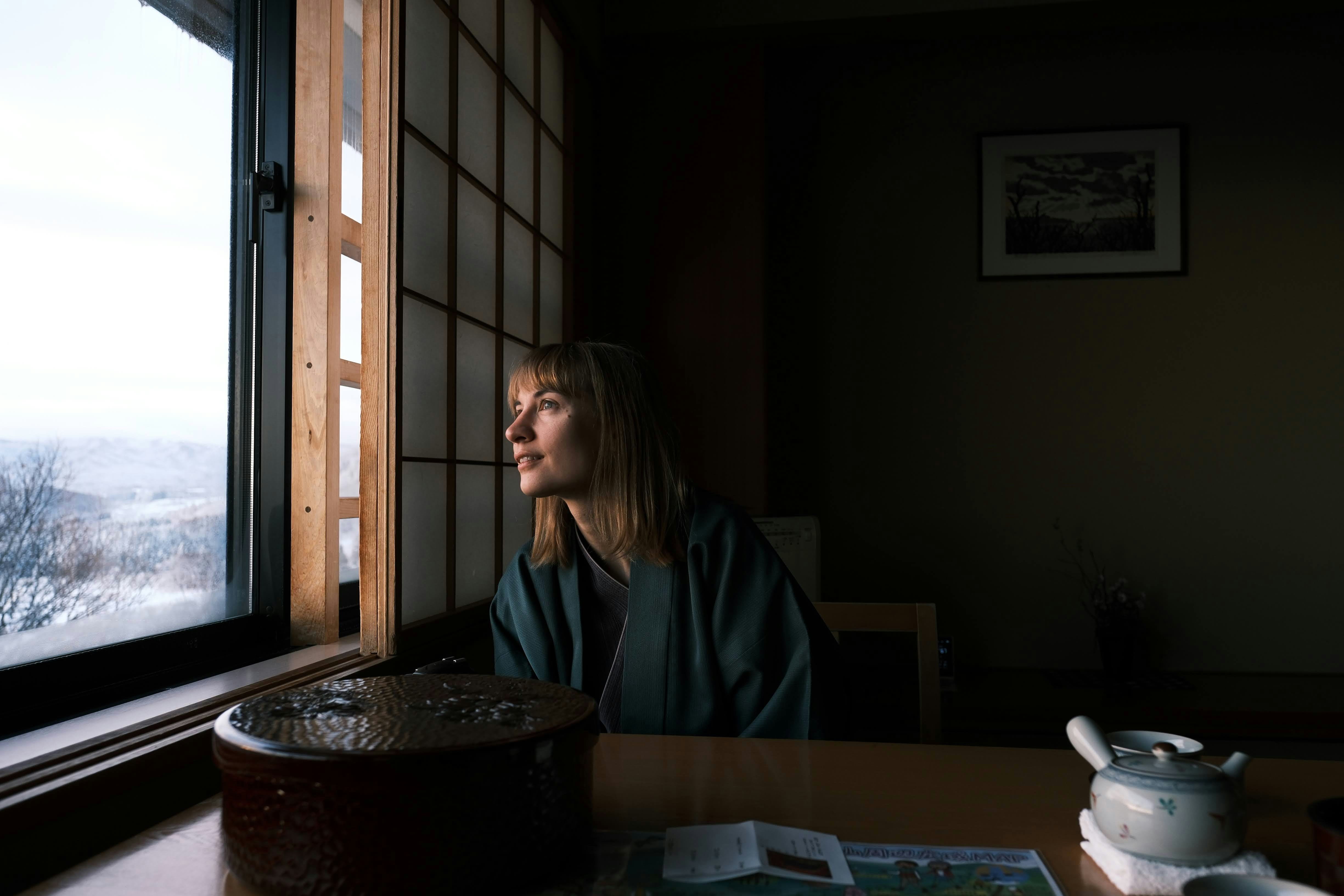 a woman sitting at a table looking out a window, 