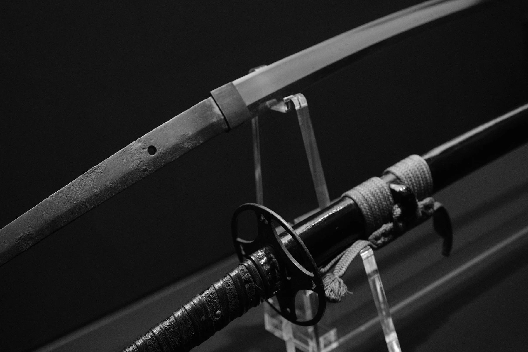 A bare Japanese blade and a mounted sword resting on clear stands, in black and white