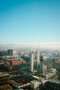 A dramatic cityscape featuring a cluster of modern skyscrapers under construction against a clear blue sky.