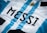 A close-up of a sports jersey featuring blue and white vertical stripes and the name 'MESSI' printed in bold black letters. A golden sun emblem is visible near the top.
