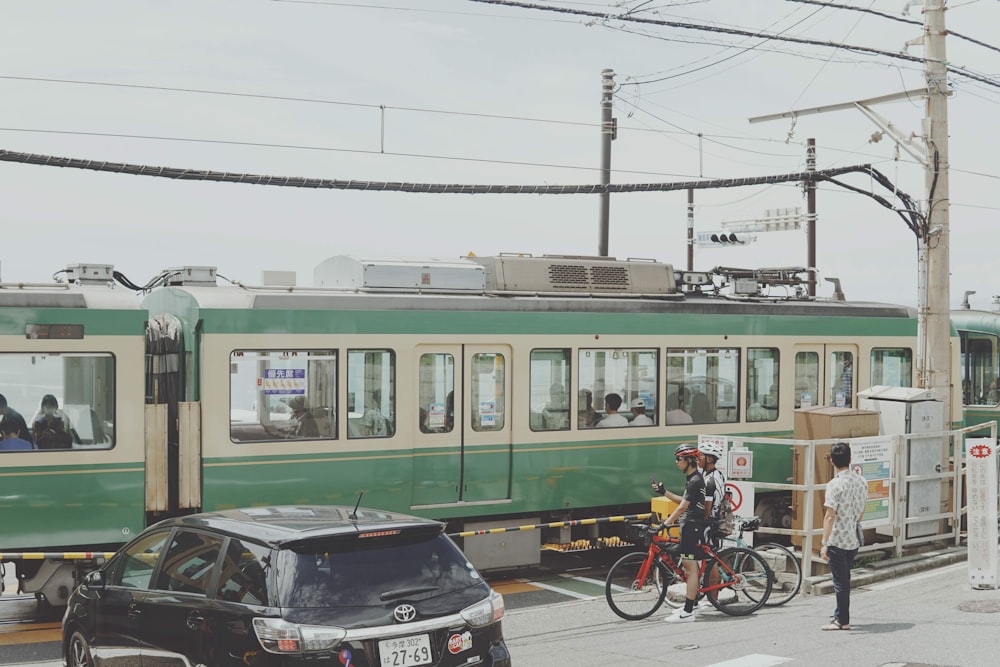 a green and white train and some cars and people