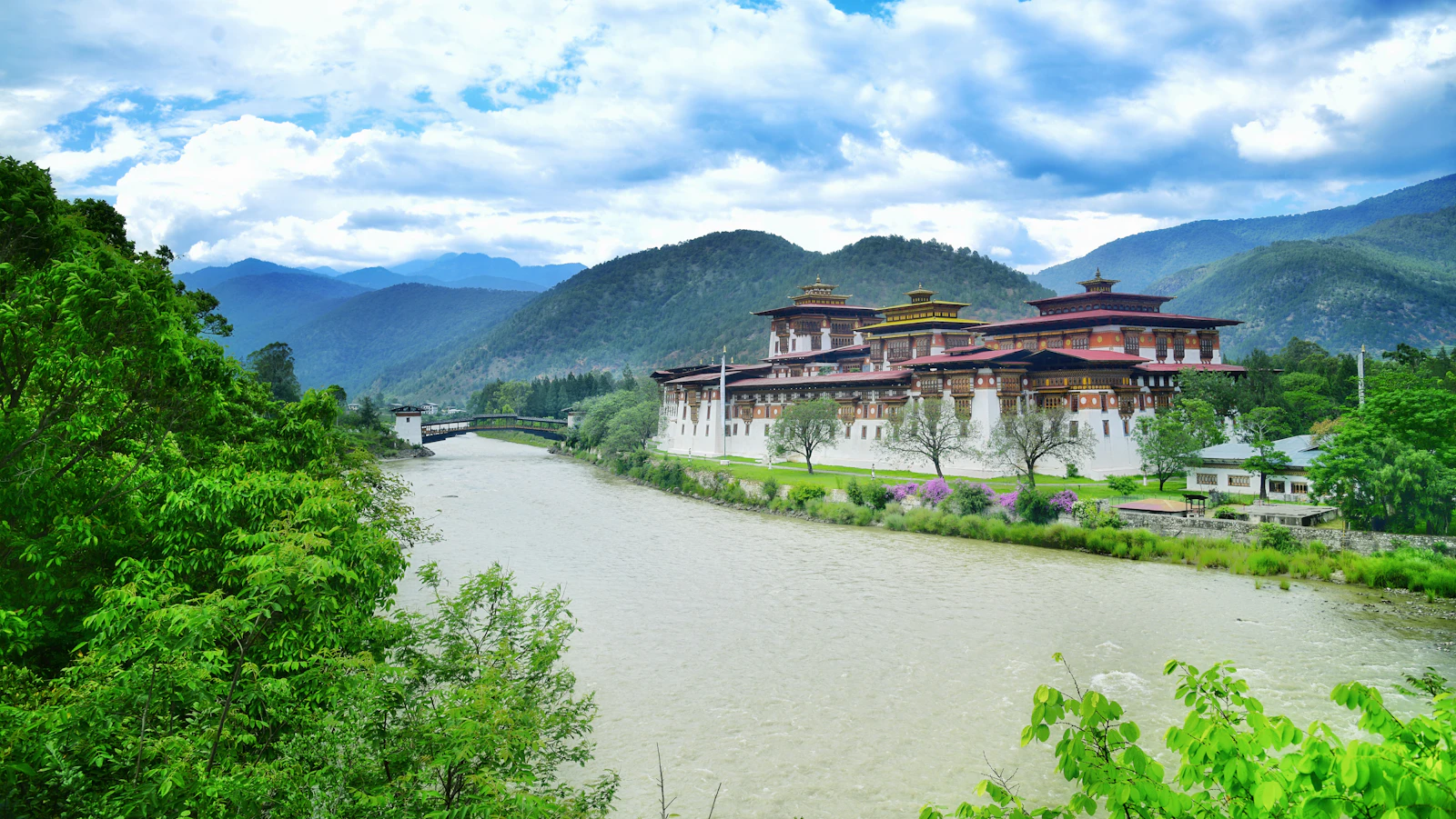 Punakha Dzong in Bhutan, its whitewashed walls and gilded roofs along the riverbank below forested hills and cloud