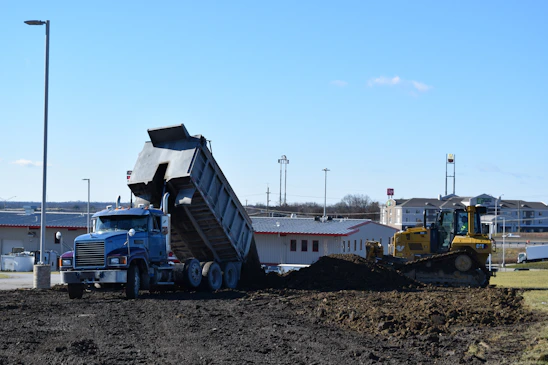 A delivery truck unloading construction materials at a busy building site under clear skies.