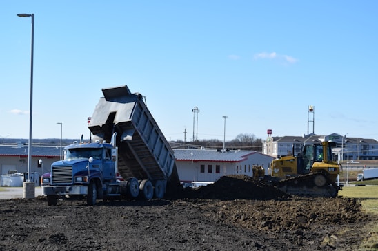 A rugged dump truck unloading dirt at a freshly cleared construction site.