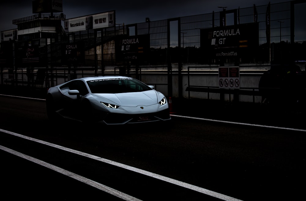 a white sports car driving down a street at night