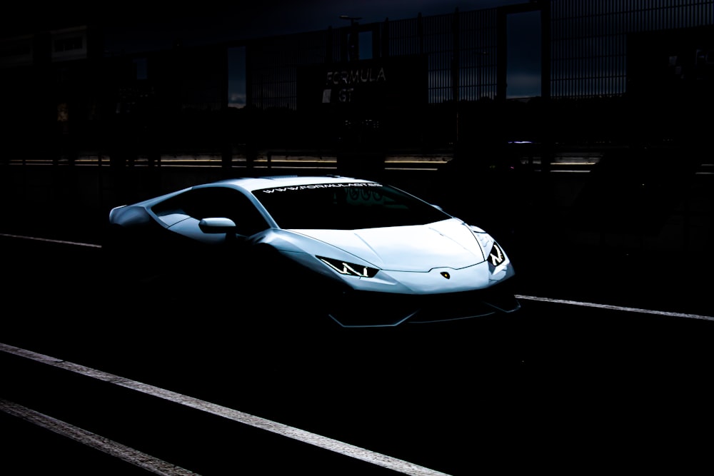 a white sports car driving down a street at night