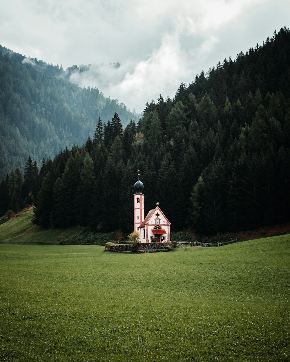a church in the middle of a field with trees in the background