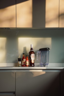 A sunlit kitchen scene with bottles of Shilp Puroc oils arranged beside fresh herbs and spices.