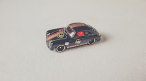 A small, detailed black toy car with gold and red stripes, placed on a light surface. It features branding and logo details that mimic a classic racing design.