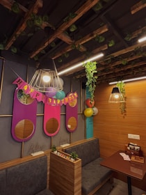 A cozy room decorated for a birthday celebration with wooden paneling and hanging lights. Vines decorate the ceiling and a 'Happy Birthday' banner is prominently displayed with colorful balloons. There are plush seating arrangements and small potted plants add a touch of greenery.