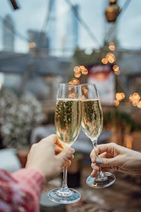 Close-up of hands holding champagne glasses with soft ivory and blush background.