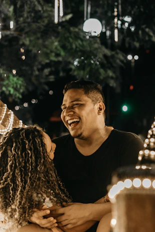A candid photo of the couple laughing together under soft fairy lights at dusk.
