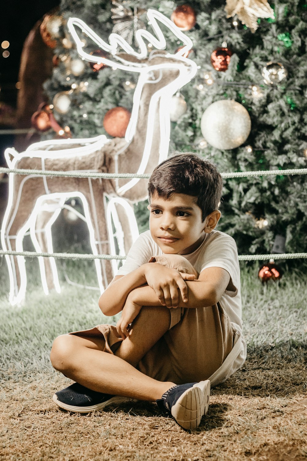a young boy sitting in front of a christmas tree