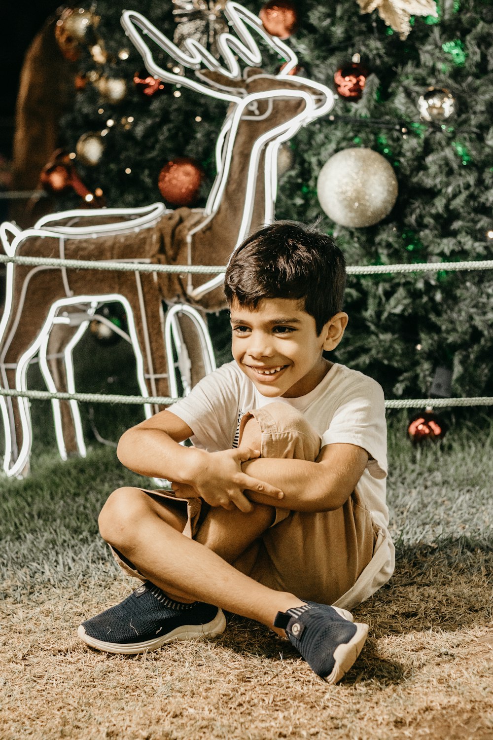 a young boy sitting in front of a christmas tree