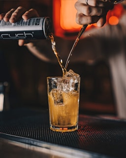 A bartender pouring a maxssala canned drink into a glass with ice.