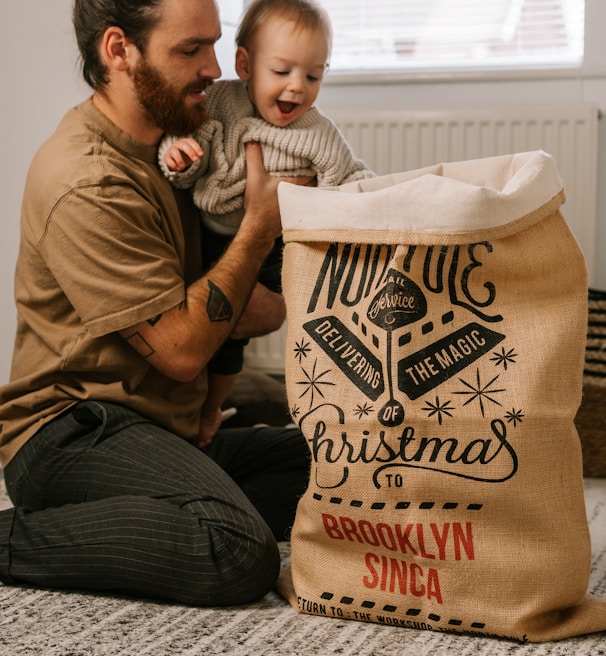 a man sitting on the floor holding a baby next to a bag