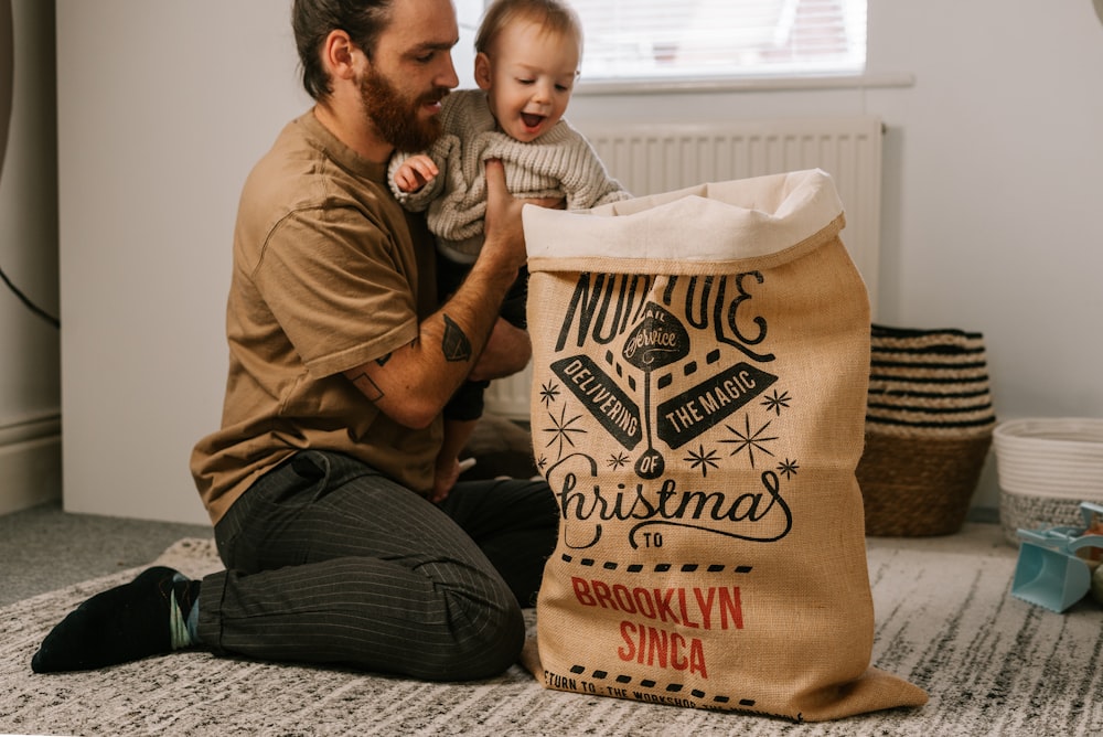 a man sitting on the floor holding a baby next to a bag