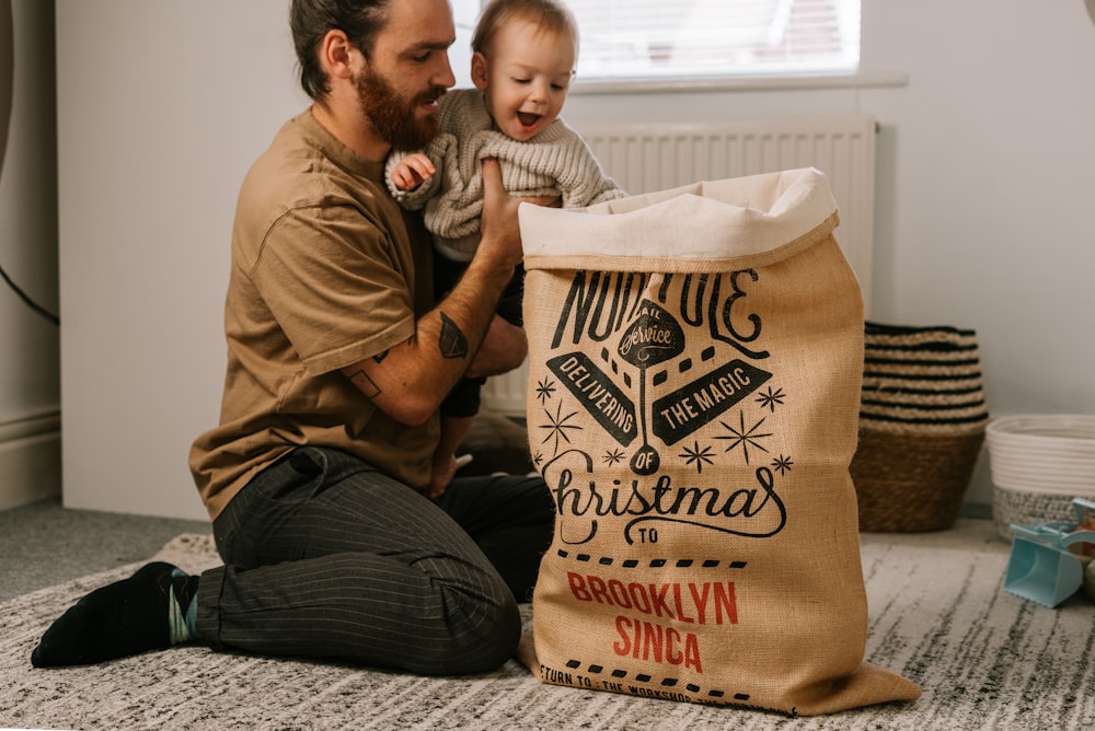 Un uomo seduto sul pavimento che tiene un bambino accanto a una borsa