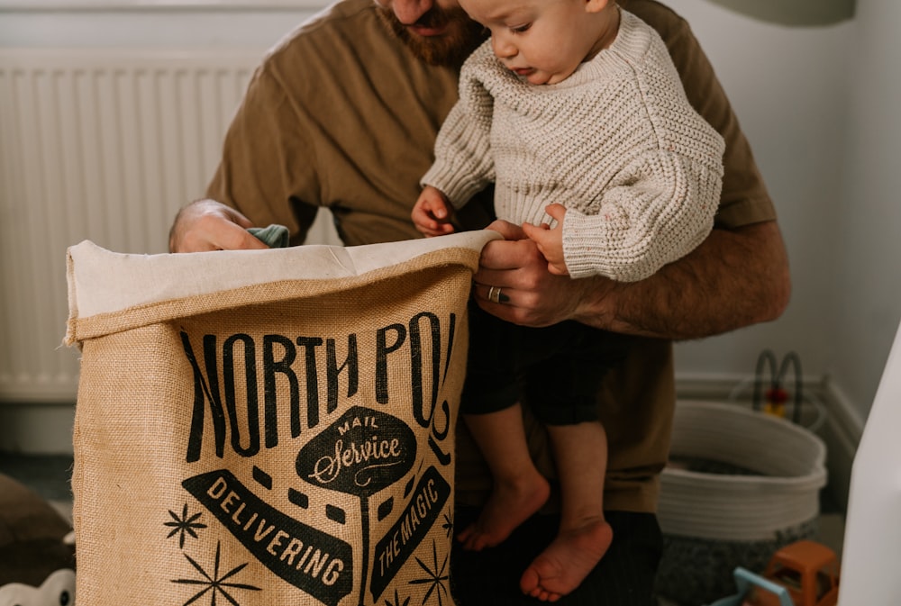 a man holding a baby next to a bag