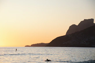 Sunset view over the calm ocean with a silhouette of a paddleboarder gliding on the water.
