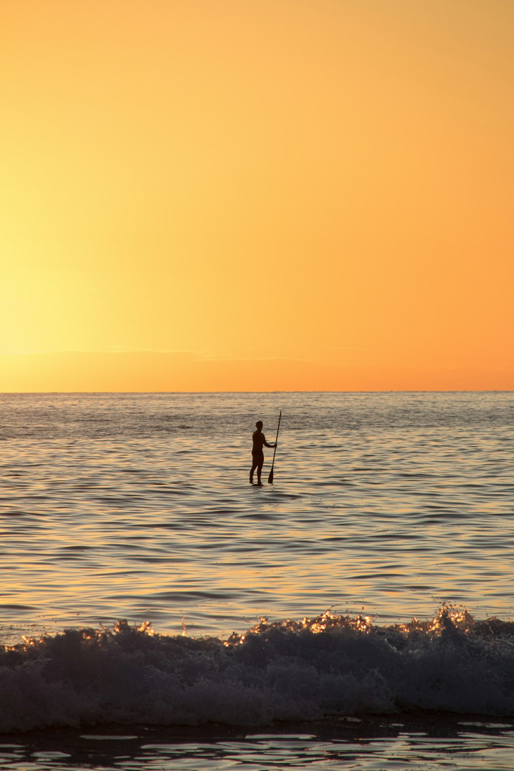 uma pessoa em uma prancha de surf no oceano ao pôr do sol