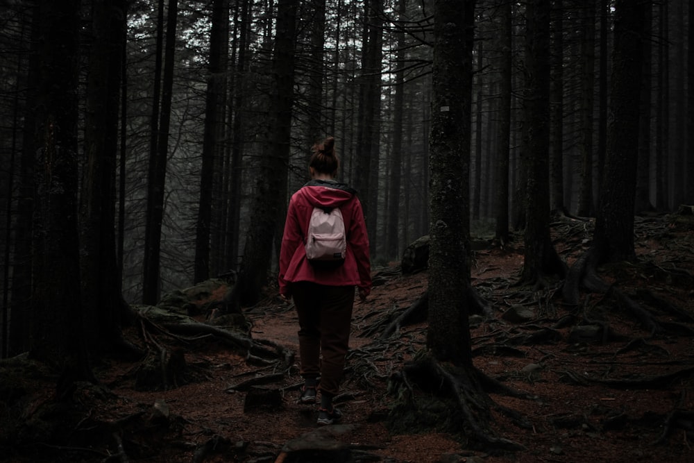 a woman in a red jacket is walking through the woods