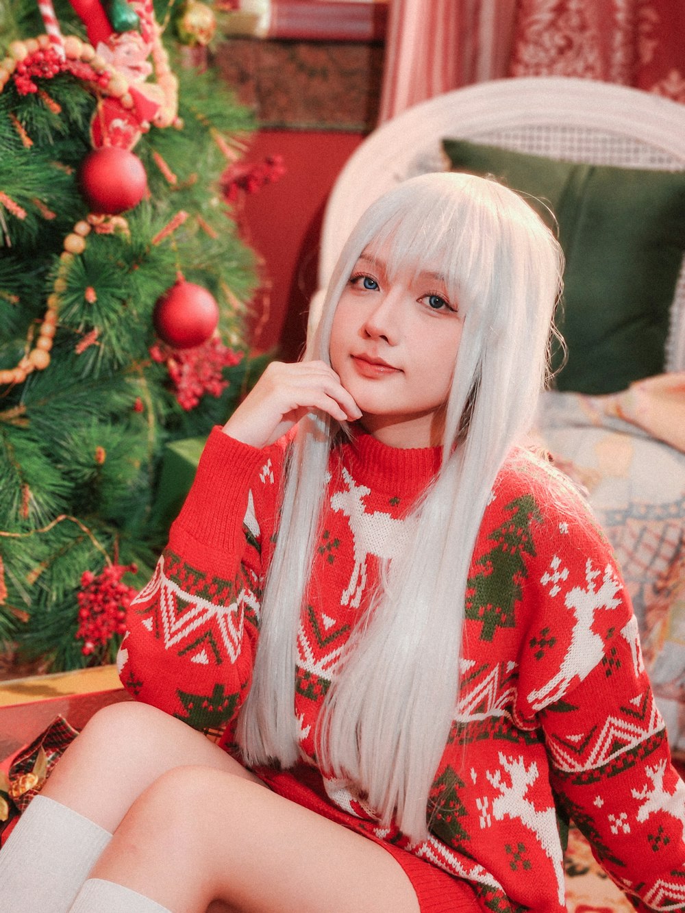 a woman with long white hair sitting in front of a christmas tree