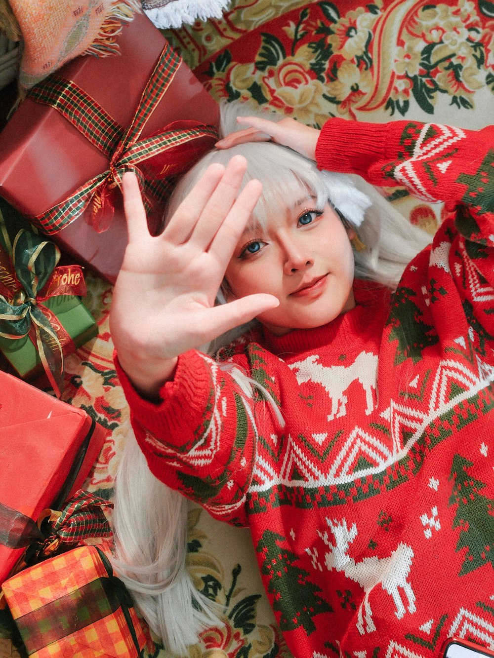 a woman in a christmas sweater holding her hand up to her face