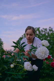 A serene homestead garden at sunset with a woman tending to her plants.