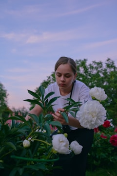 A serene homestead garden at sunset with a woman tending to her plants.