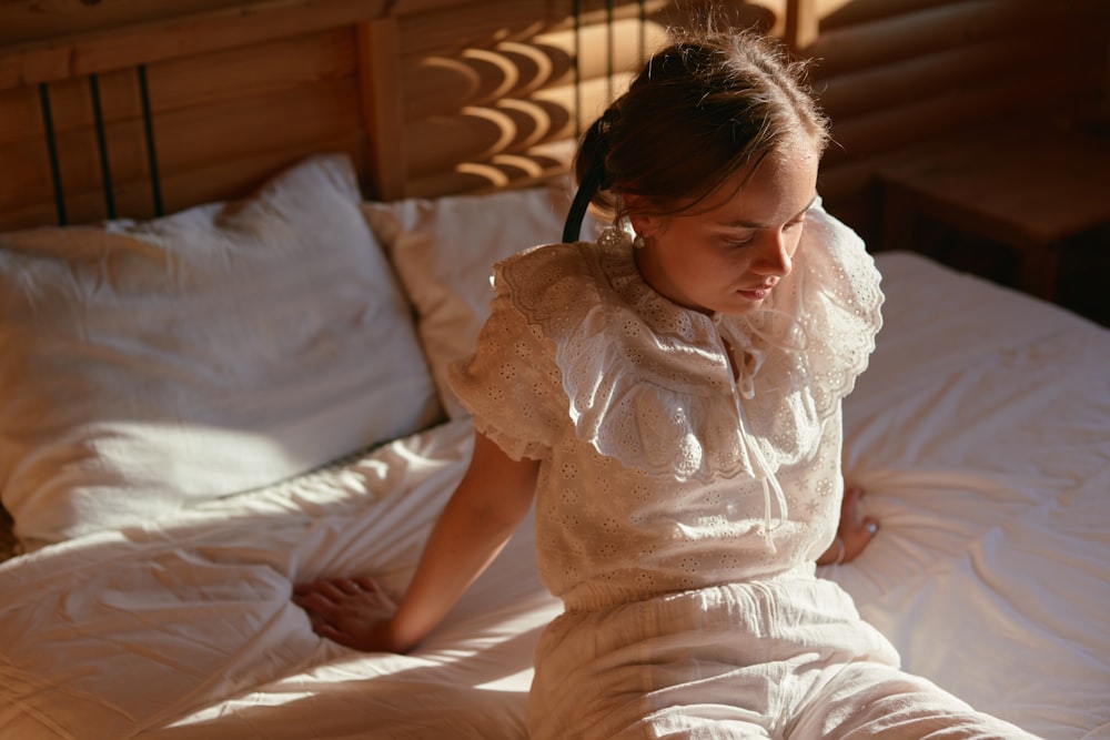 a young girl sitting on a bed with white sheets